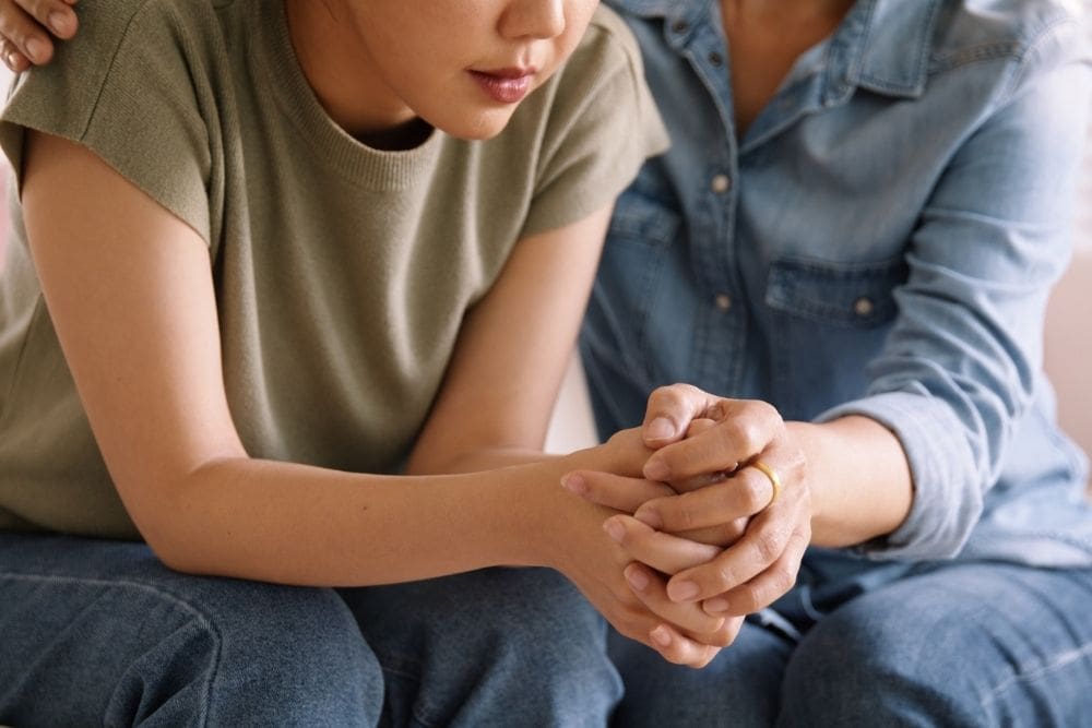 Two people sitting closely together, one offering comfort with a hand on the other's shoulder, conveying support and empathy during a difficult moment.