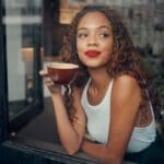 Creekside - How to Navigate Days When Everything Feels Overwhelming. A young woman stres into the distance as she holds a cup of coffee from her lips. Woman appears content in a modern looking room.