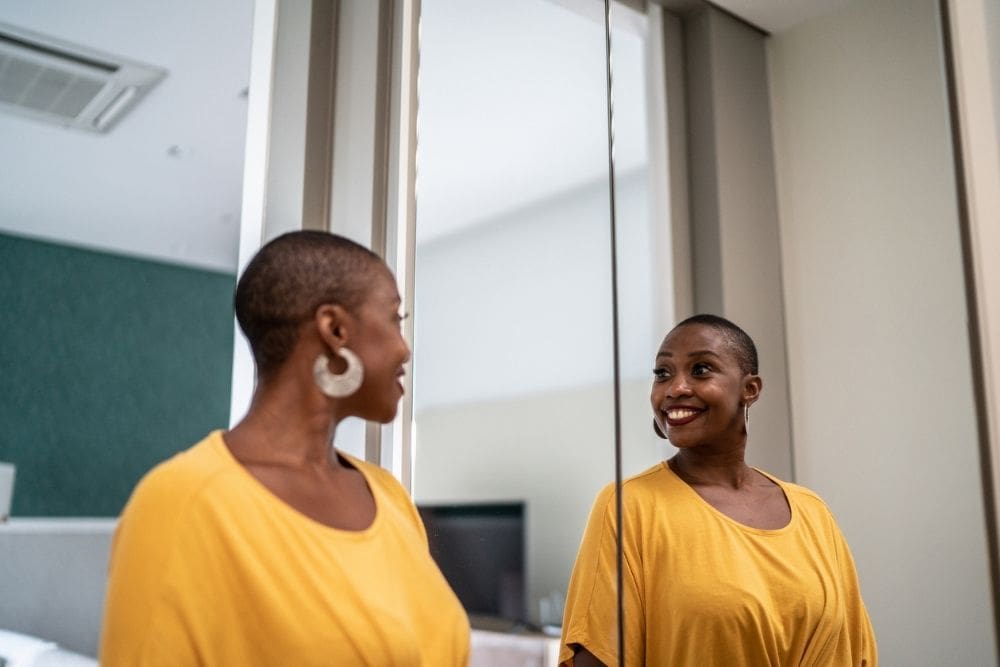 Person smiling at their reflection in a mirror, practicing positive self-talk in a calm indoor setting.