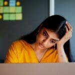 Creekside - How to Stop Negative Thinking - Edited. A frustrated woman sits at a computer with her head in her hand.